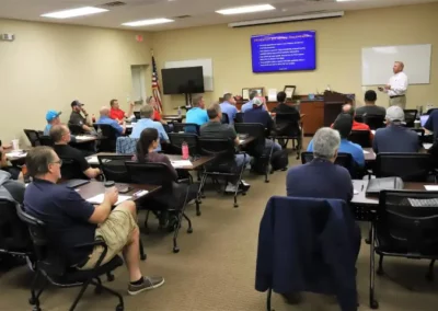 A large group of home inspectors sits in a room learning from an instructor